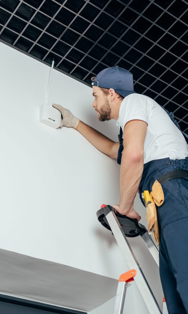 low angle view of young electrician fixing home alarm