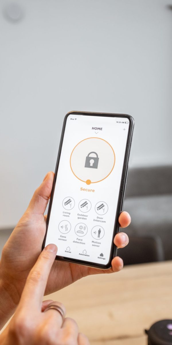 Holding a smartphone with launched security program indoors. Concept of controlling and managing home security from a mobile device